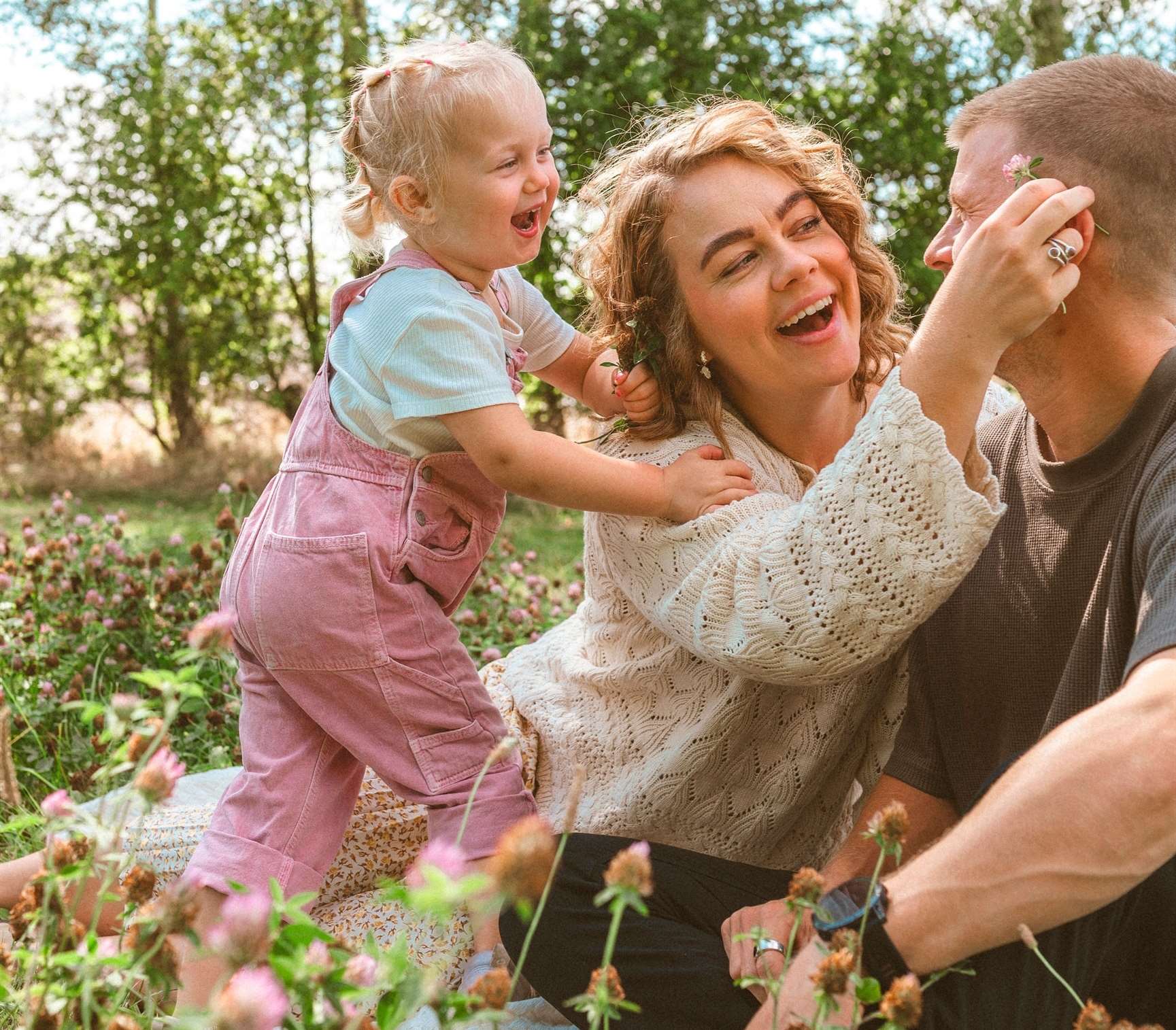 Børnefotografi i naturen taget af professionel børnefotograf i Odense. Forældre og barn griner og leger i en blomstereng en solrig dag.